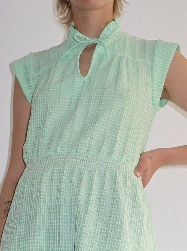Vintage semi sheer green check striped summer dress. Soft tie at neck with a lovely ruffle collar. Short capped sleeves with an elastic waist and fall at the knee. Classic 60s textured fabric with a slight stretch.