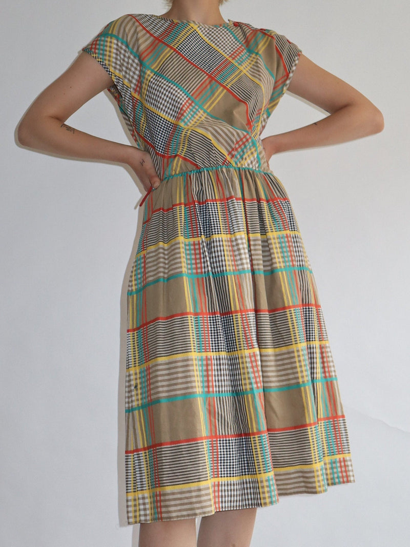 Snap red button detail with beautiful yellow on a brown plaid print dress. Pockets with a stretchy waist. Short capped sleeves in a relaxed fit. A fun summer festival weekend party dress.