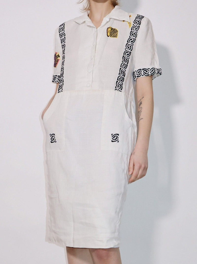 White summer cotton dress. Classic front collar, embroidered details throughout, and two front pockets. Slim fit with short sleeves.