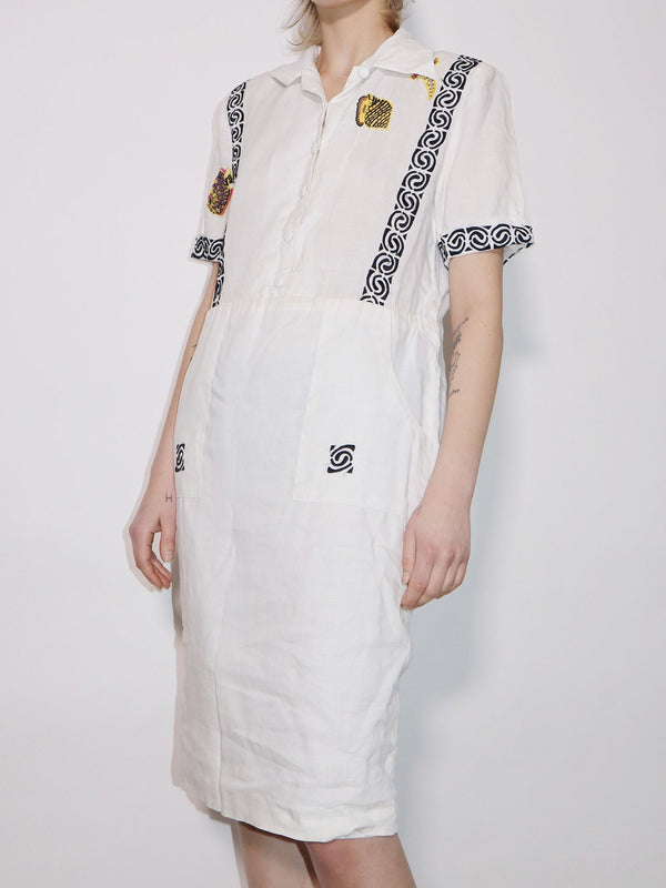 White summer cotton dress. Classic front collar, embroidered details throughout, and two front pockets. Slim fit with short sleeves.